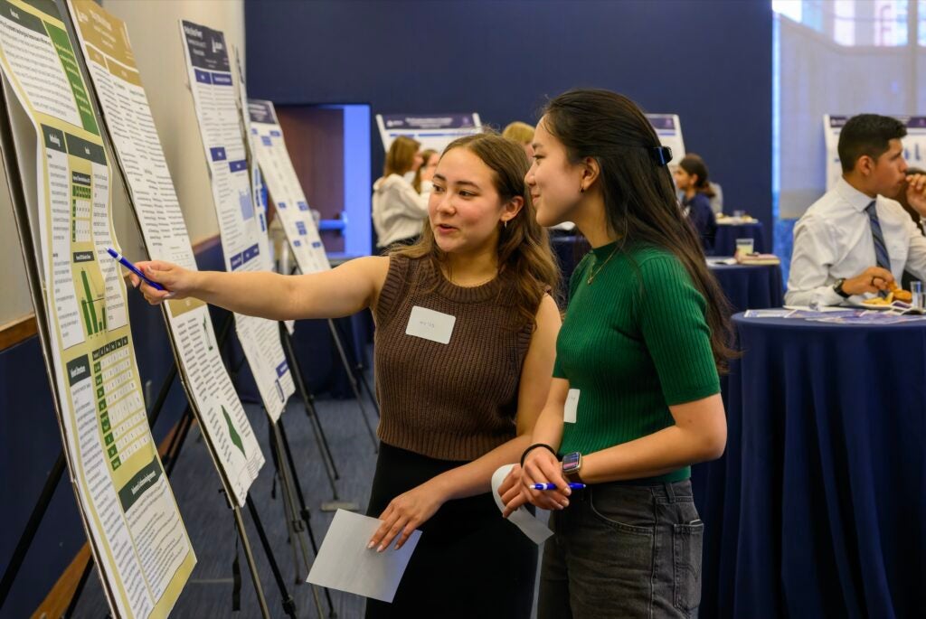 Two young women read a poster situated in front of them on an easel.